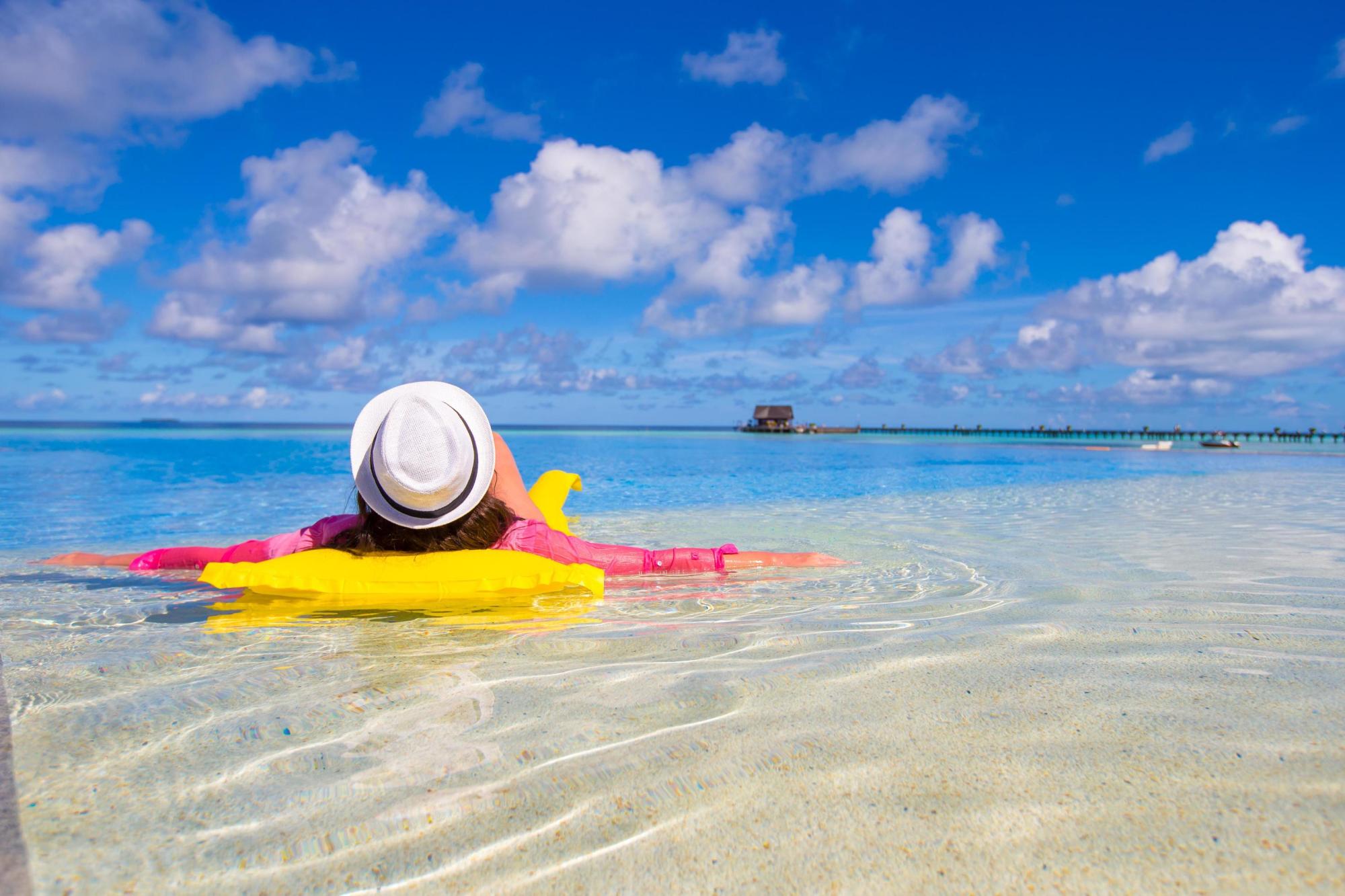 Person relaxing on yellow float in clear ocean under a blue sky with clouds.