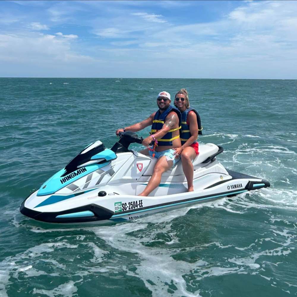 Two people on a jet ski in the ocean, under a clear blue sky.