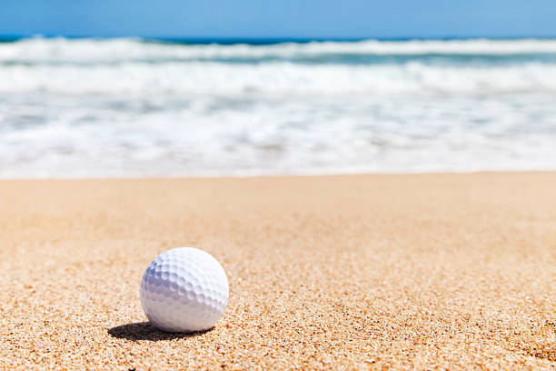 Golf ball on sandy beach with ocean waves in the background.