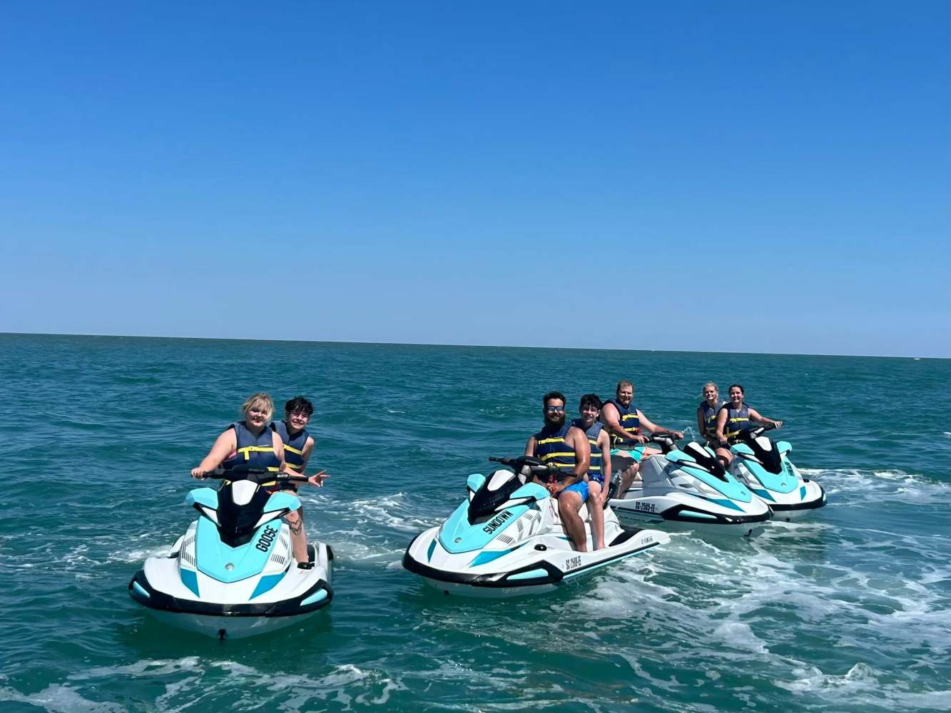 Group of six people riding jet skis on the ocean under a clear blue sky.