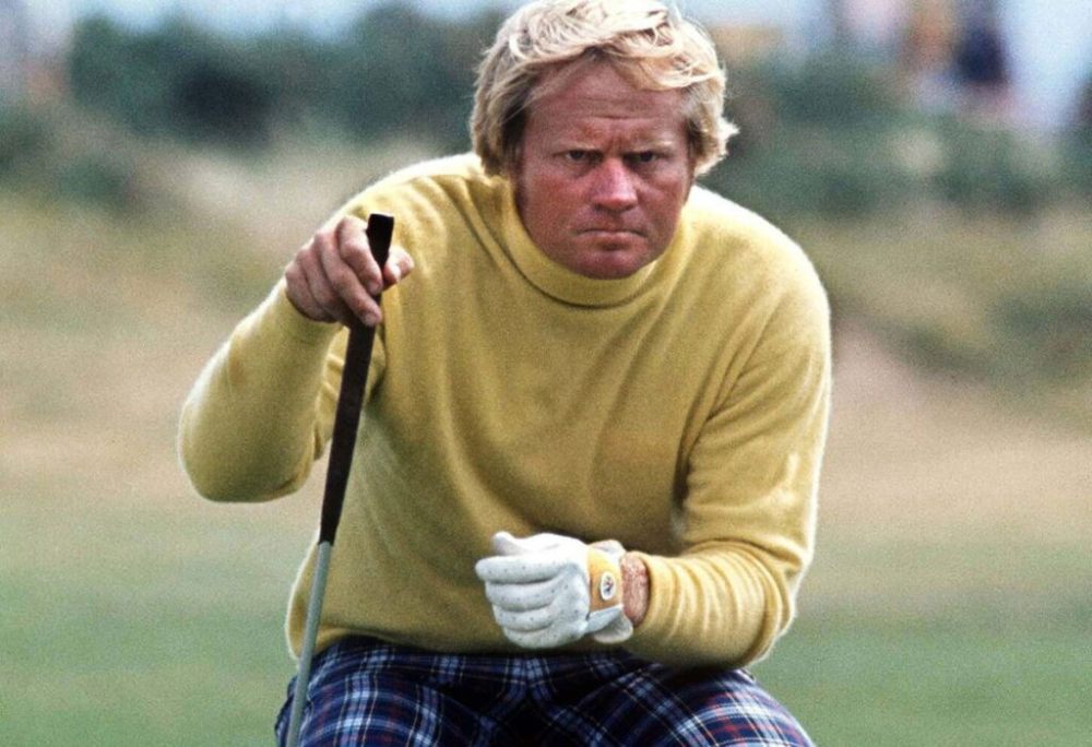 Golfer in yellow sweater and plaid pants crouching on a golf course, focusing on a putt.