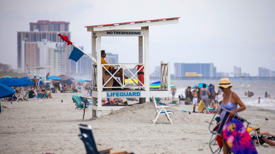 Crowded beach with lifeguard tower and colorful umbrellas.