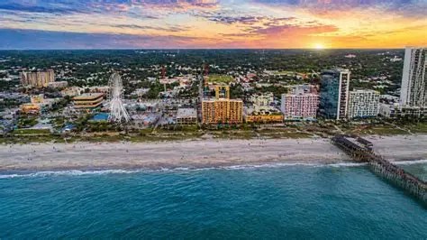 Aerial view of a beachfront cityscape with a pier at sunset.