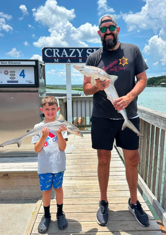 Man and boy holding fish on a marina dock under a blue sky.