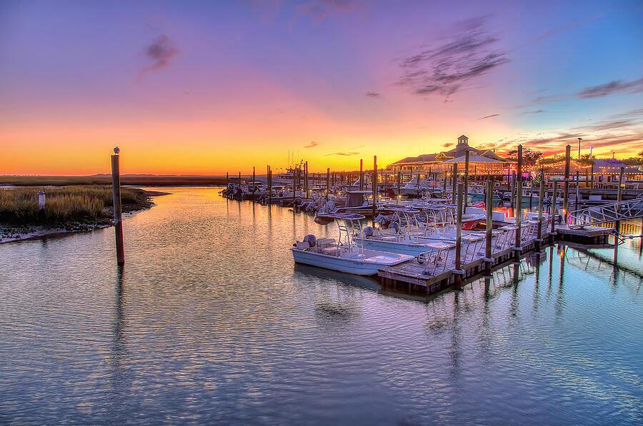 Sunset over a marina with boats docked, calm water, and colorful sky.