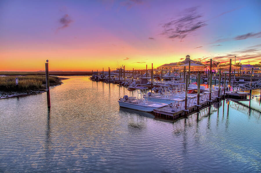 Sunset over a marina with boats docked, calm water, and colorful sky.
