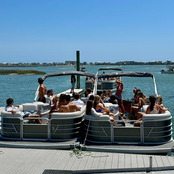 Groups of people sitting on pontoon boats at a dock by the water.