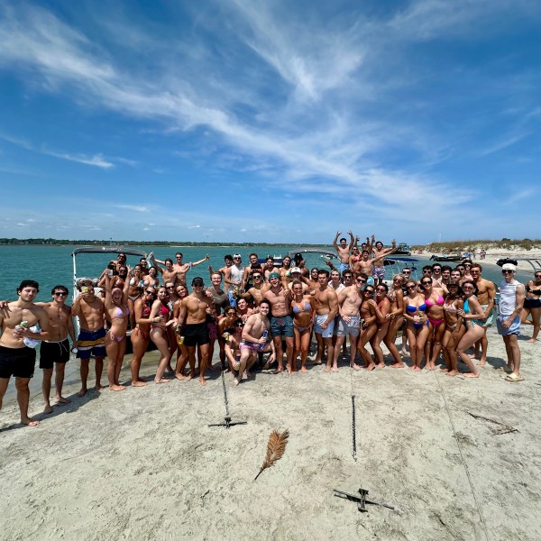 Large group of people posing on a beach, with the sea in the background.