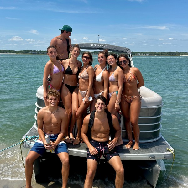 Group of people in swimwear posing on a boat by the water.