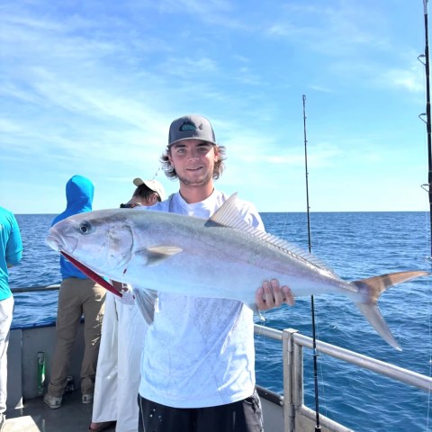Man on boat holding large fish with ocean in background.
