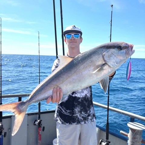Person holding a large fish on a boat with ocean in background.