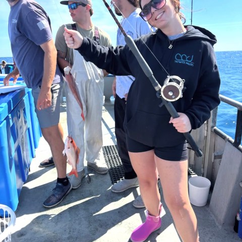 Smiling woman holds fishing rod, others around with caught fish on boat.