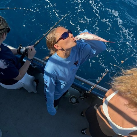 Person on boat kisses fish, with ocean in background.