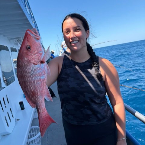 Person holding a red snapper fish on a boat with the ocean in the background.